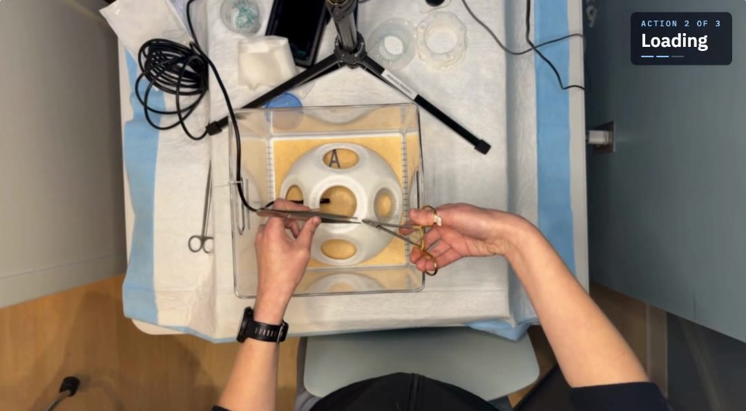 Overhead view of a resident suturing at the station, with the current action labeled